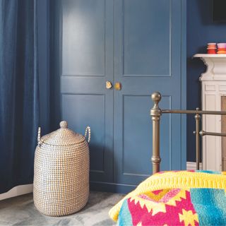 Bedroom with blue wardrobe and matching blue curtains, a metal framed bed and a wicker storage basket on the floor