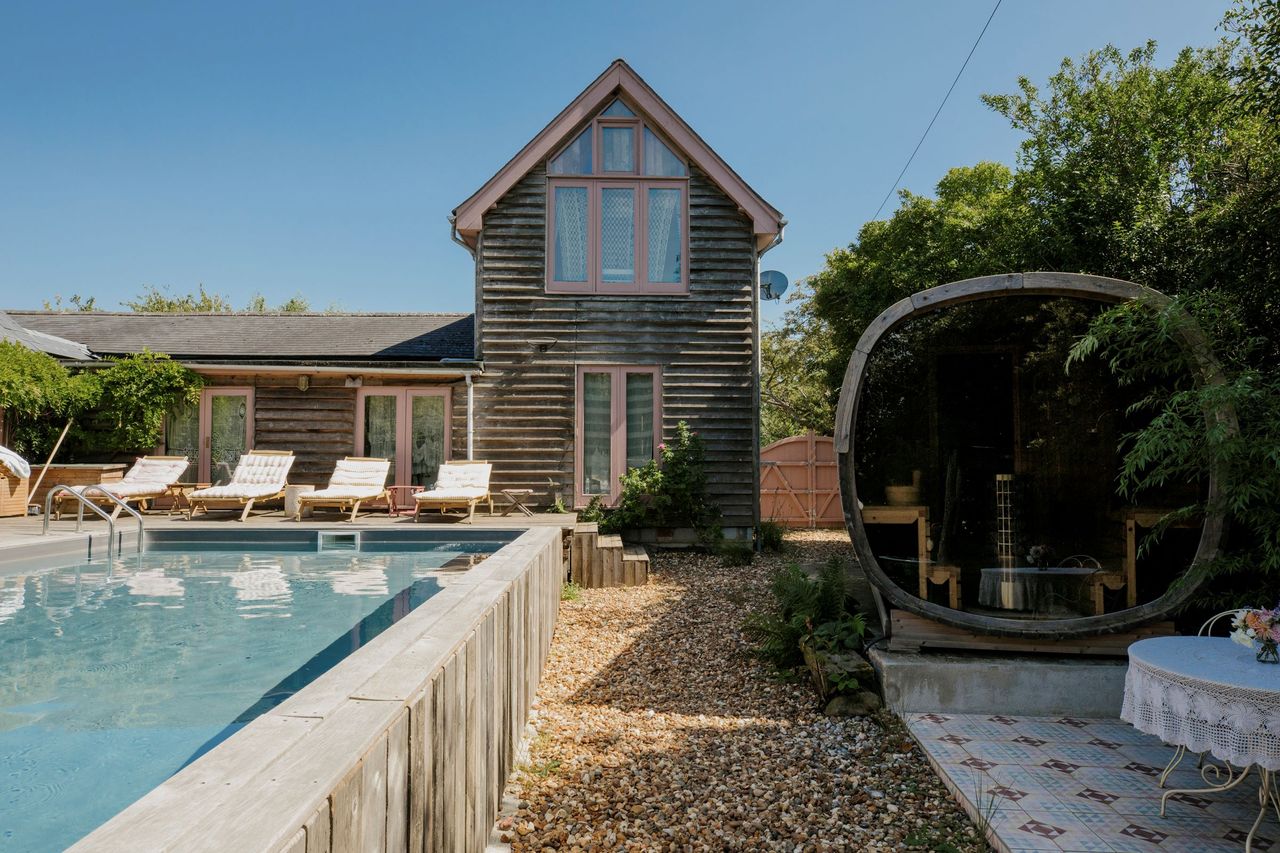 A raised swimming pool sits in the back garden with a private sitting area in a large wooden egg chair sit next to the pool