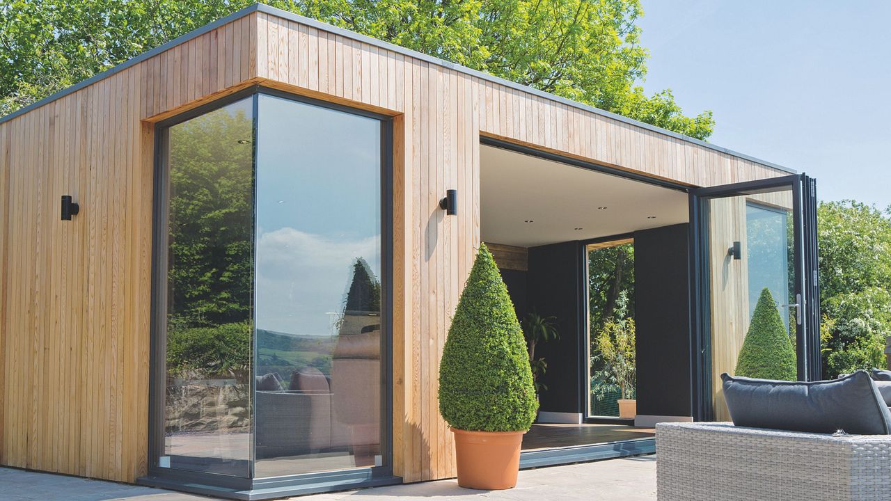 Modern garden room with wooden exterior, windows and potted tree