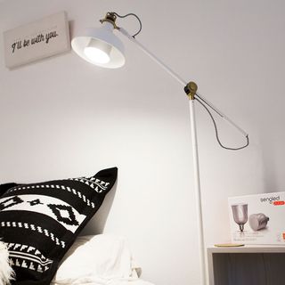 A white standard lamp next to a bed with a black and white pillow