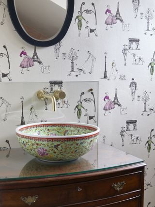 Parisian-inspired wallpaper with patterned bathroom counter top basin, vintage chest and gold plated faucets