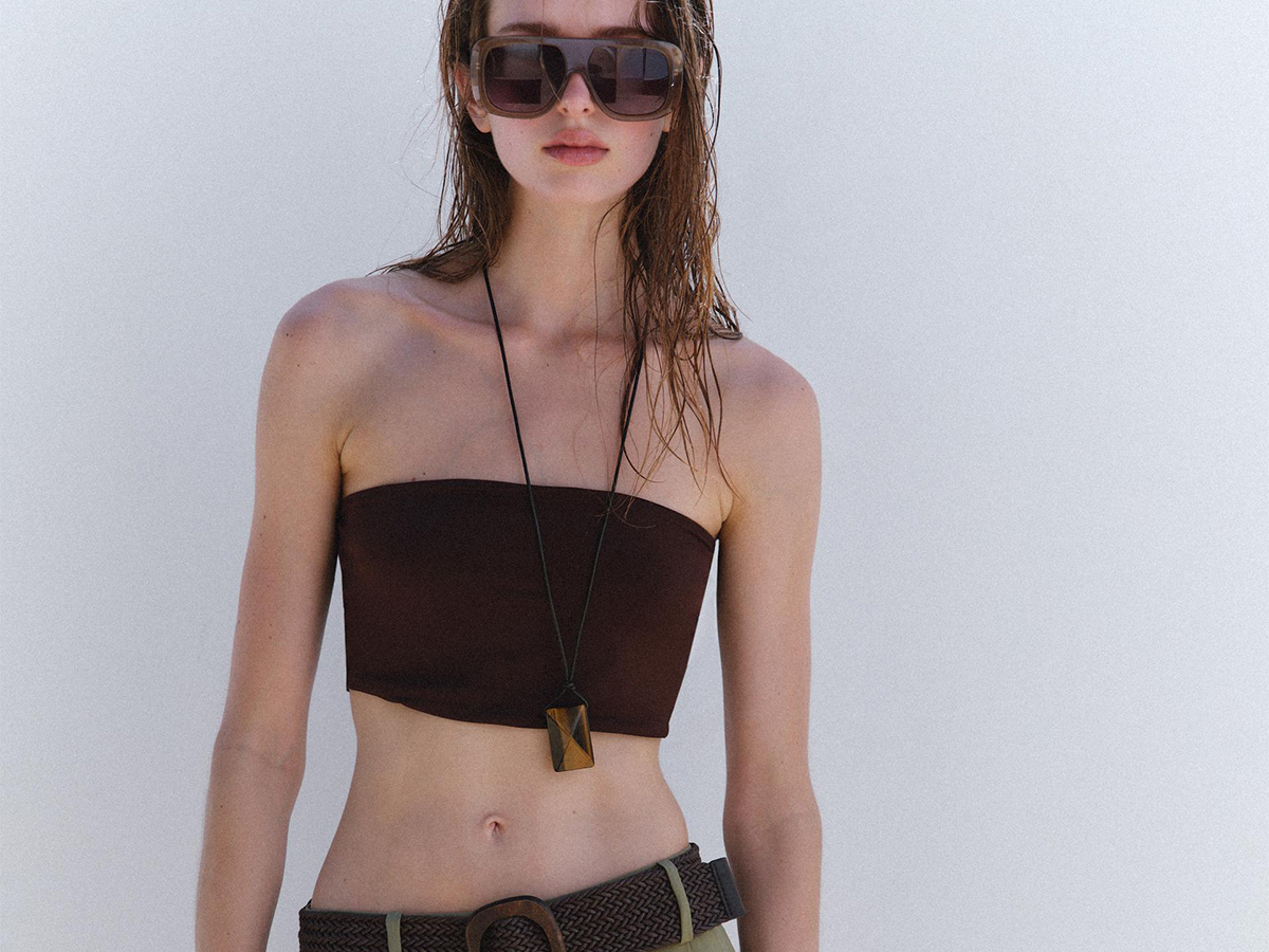 Zara model wearing pleated belt short, brown tube top, and oversized sunglasses.