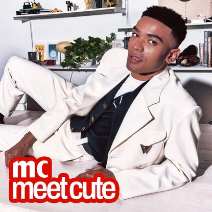 Owen Thiele poses in a white suit with a black vest underneath lying on a counter in an office for marie claire's meet cute series