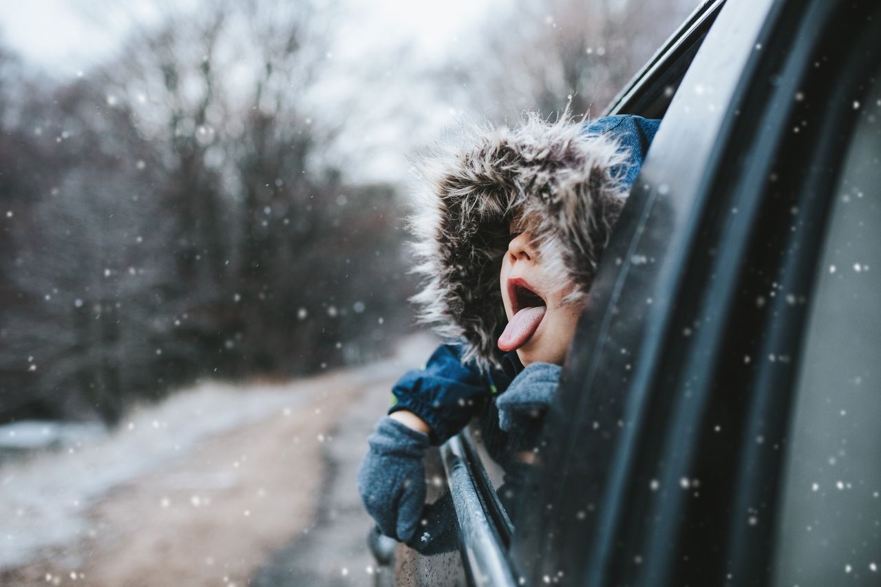 Boy on a road trip. the little boy is looking from the car window in winter , opened his mouth and pulled out his tongue, catches snowflakes