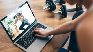 Woman doing strength training on laptop with dumbbells to beat weight loss plateau