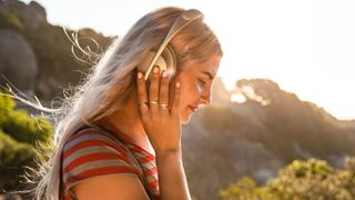 En kvinde, der lytter til podcasts ude i naturen med et par hvide hovedtelefoner
