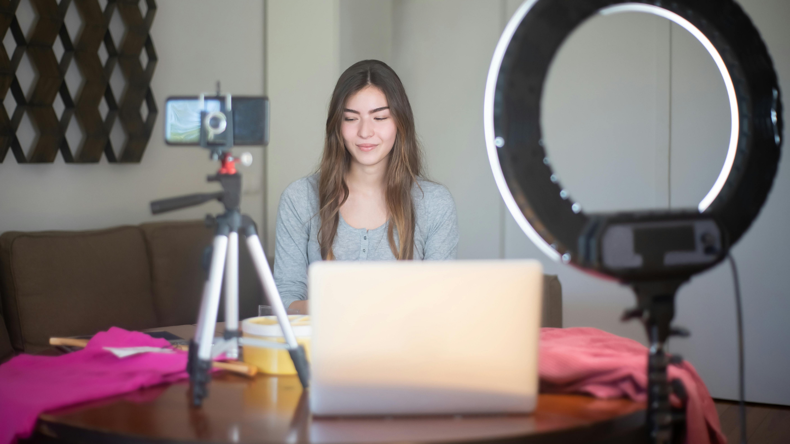 A woman in front of a camera, ring light, and laptop making videos