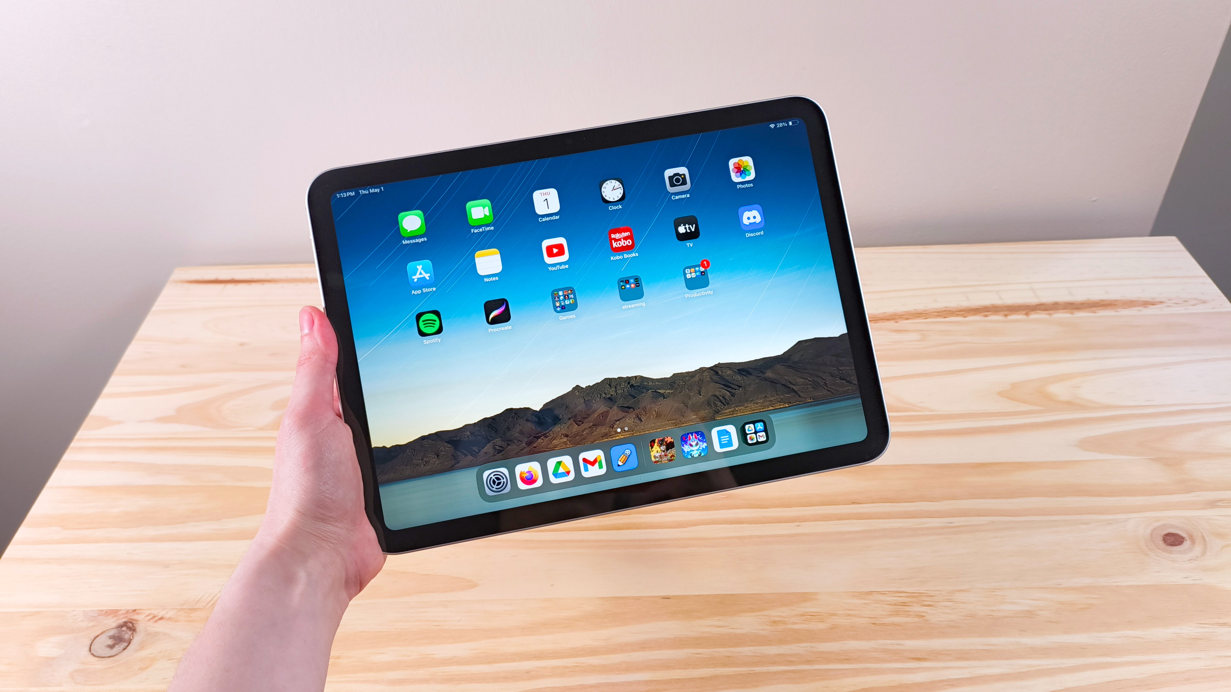 A hand holding up the iPad 11 showing the home screen