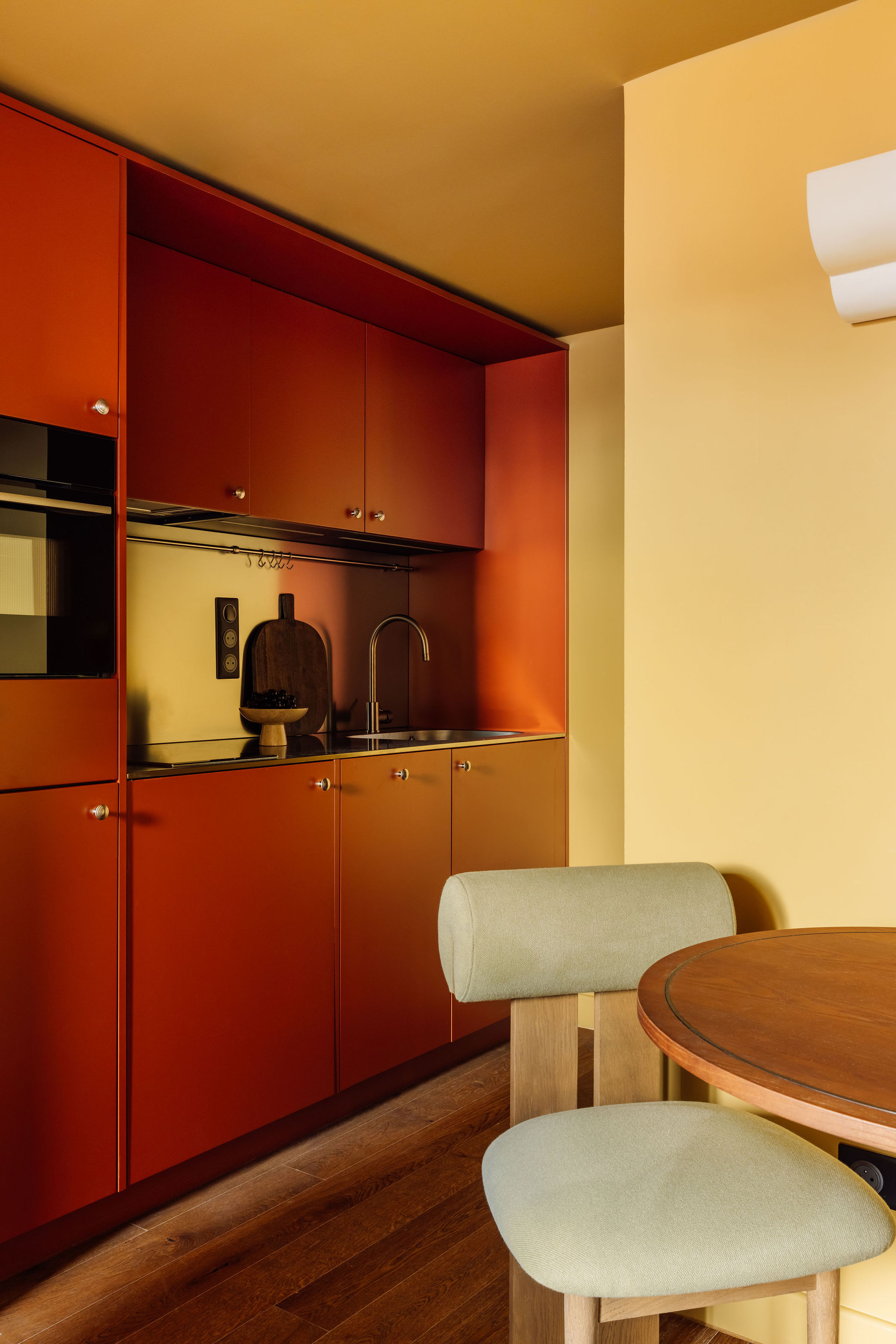 A vibrantly decorated hotel room boasts color-blocked walls n the tones of butter, orange, beige, and coral, sculptural furniture with a whimsical touch, and abstract artwork.