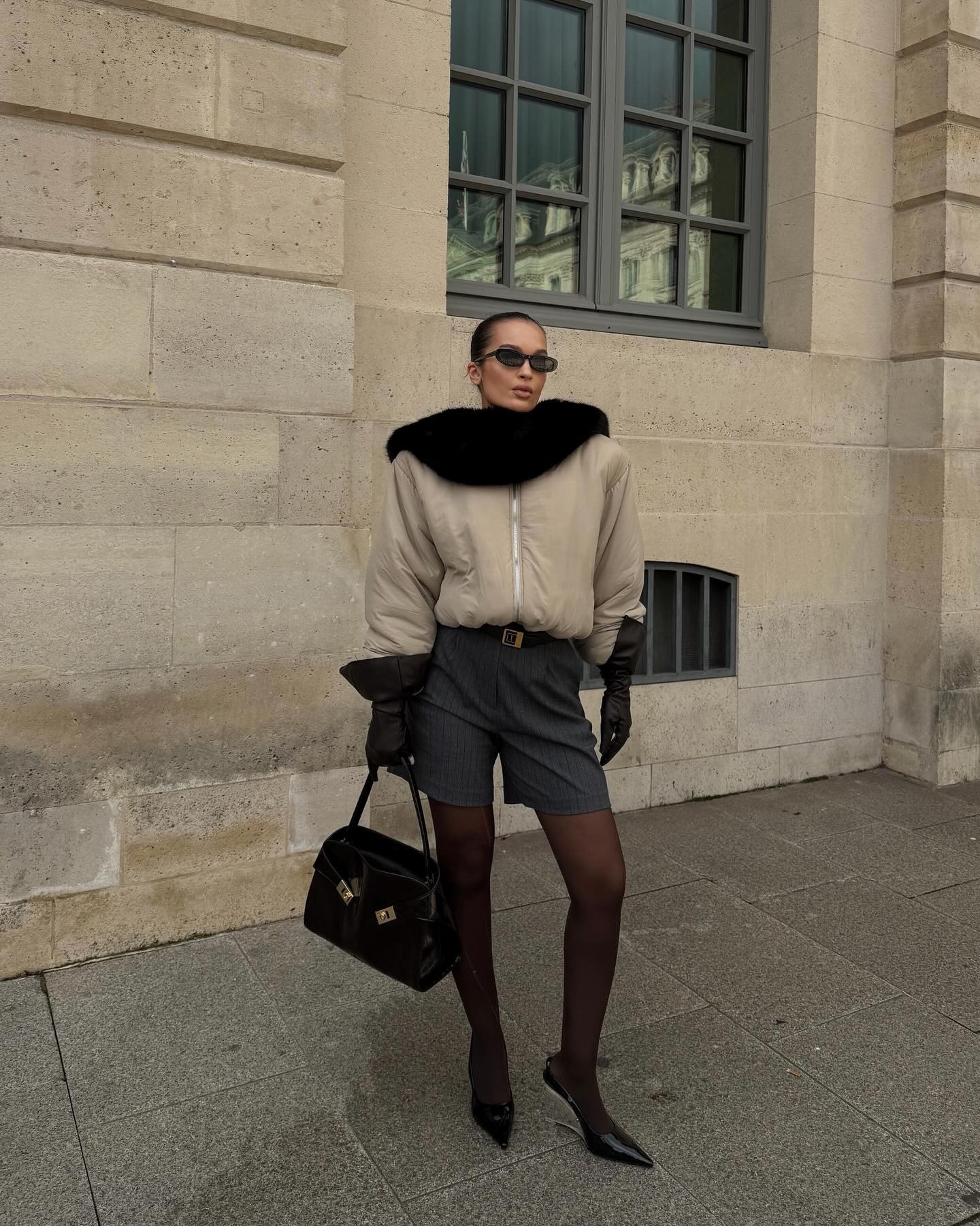 @oumaymaboumeshouli wears a black fur scarf over a bomber jacket with Bermuda shorts, sheer tights, heels, and black leather gloves.