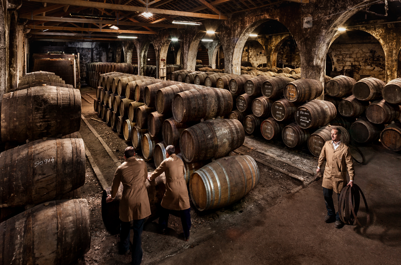 A Port barrel cellar with rows of barrels and three cellarmen walking between teh rows