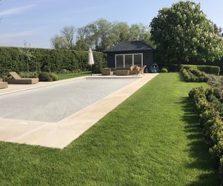 A rectangular pool set into a lawn surrounded by topiary hedges and formal evergreens