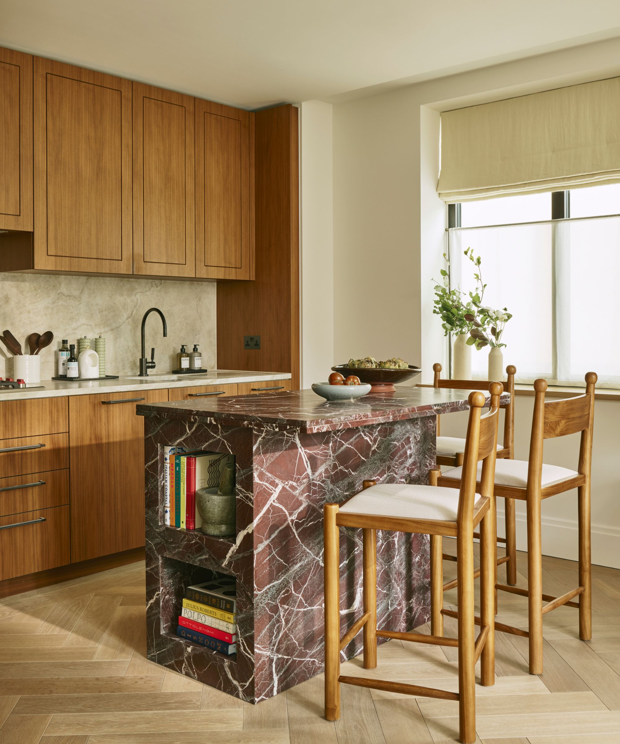a warm oak flat paneled small kitchen with a small rosso red marble island and oak bar stools