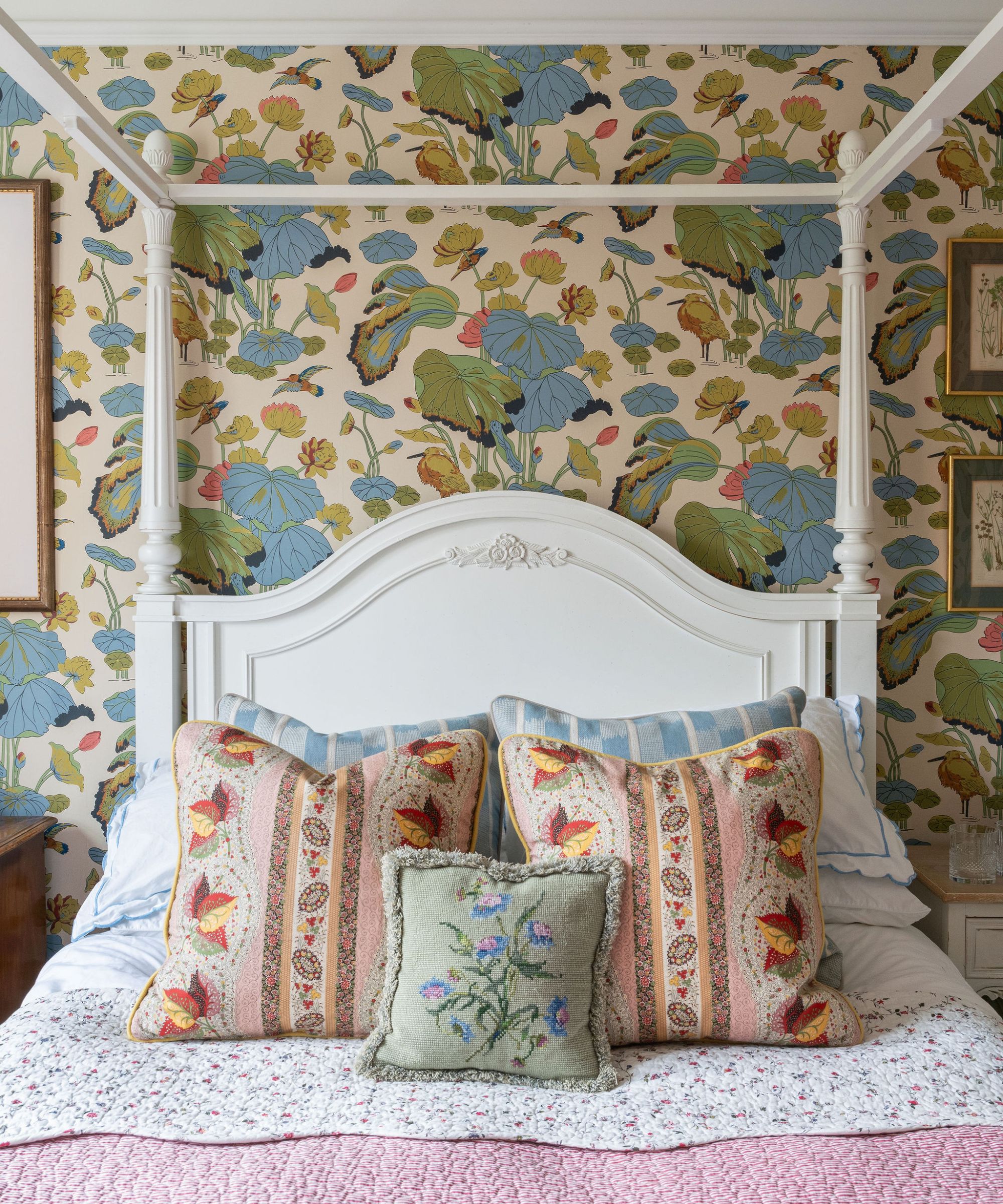 bedroom with floral wallpaper, patterned bedding, colorful cushions, and a four-poster bed