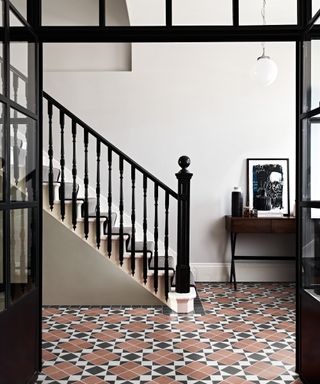 hallway with terracotta, black and white floor tiles, black framed doors and black painted staircase