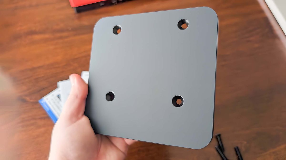 A hand holding the JSAUX VESA adapter to show off its rubber underside.