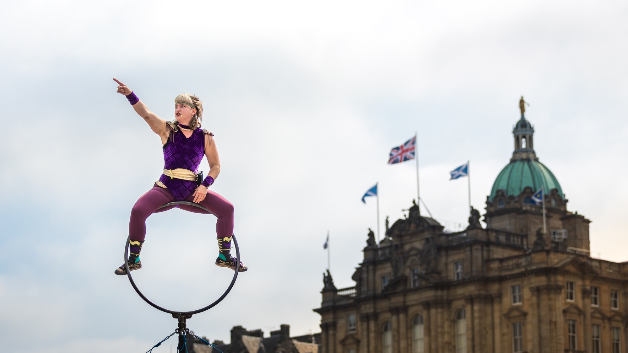 Street acrobat performer resting on a pole with Edinburgh city in the background
