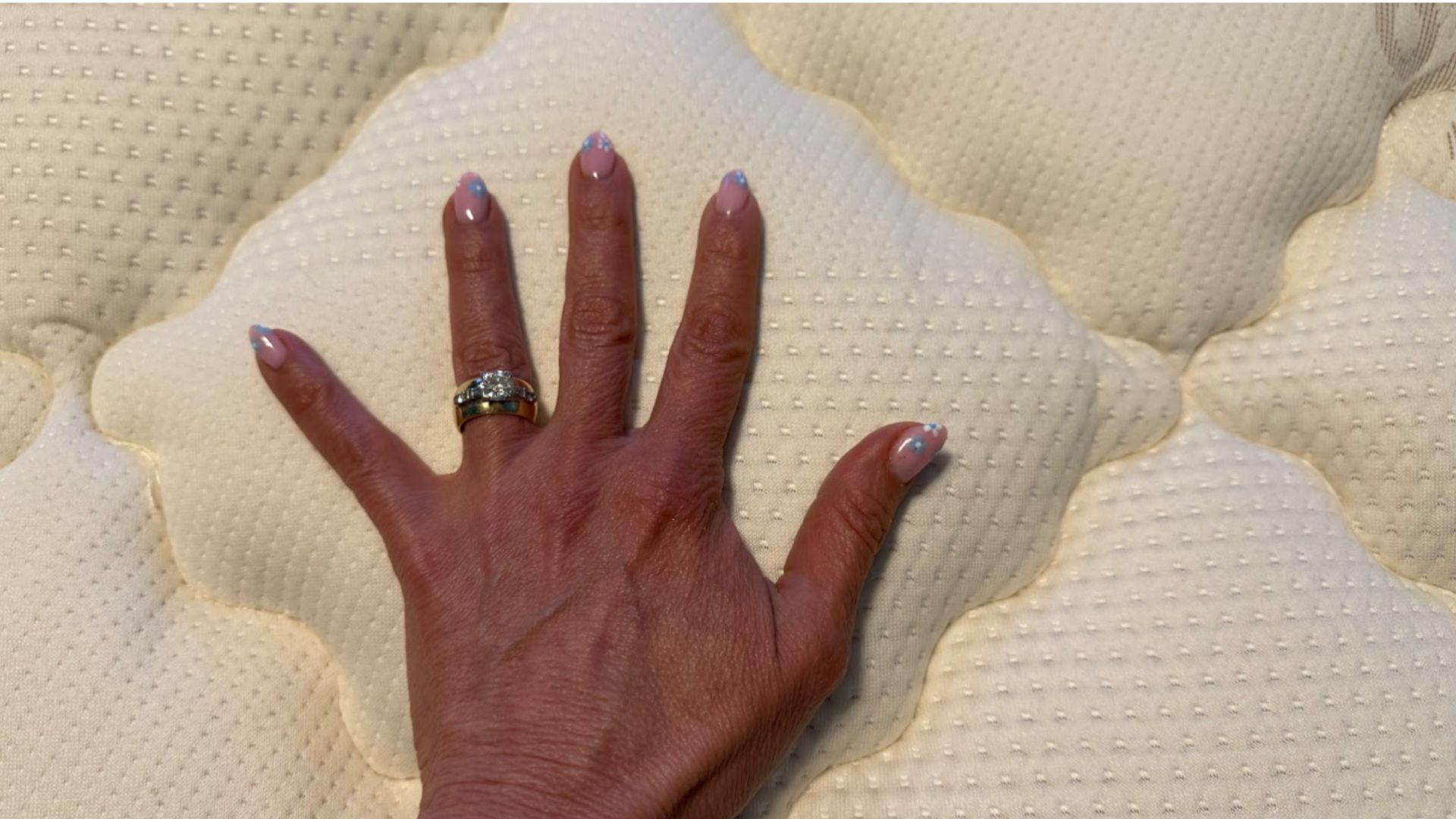 A woman&#039;s hand with wedding rings resting on Saatva Solaire mattress to check temperature