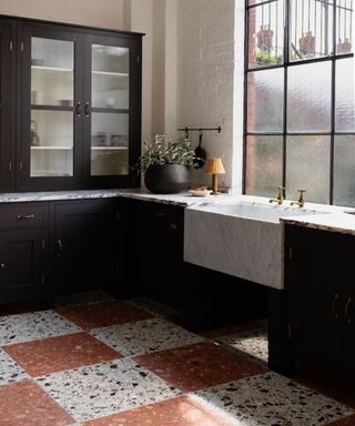 A kitchen with white countertops and black cabinets, and a white and pink terrazzo tile floor