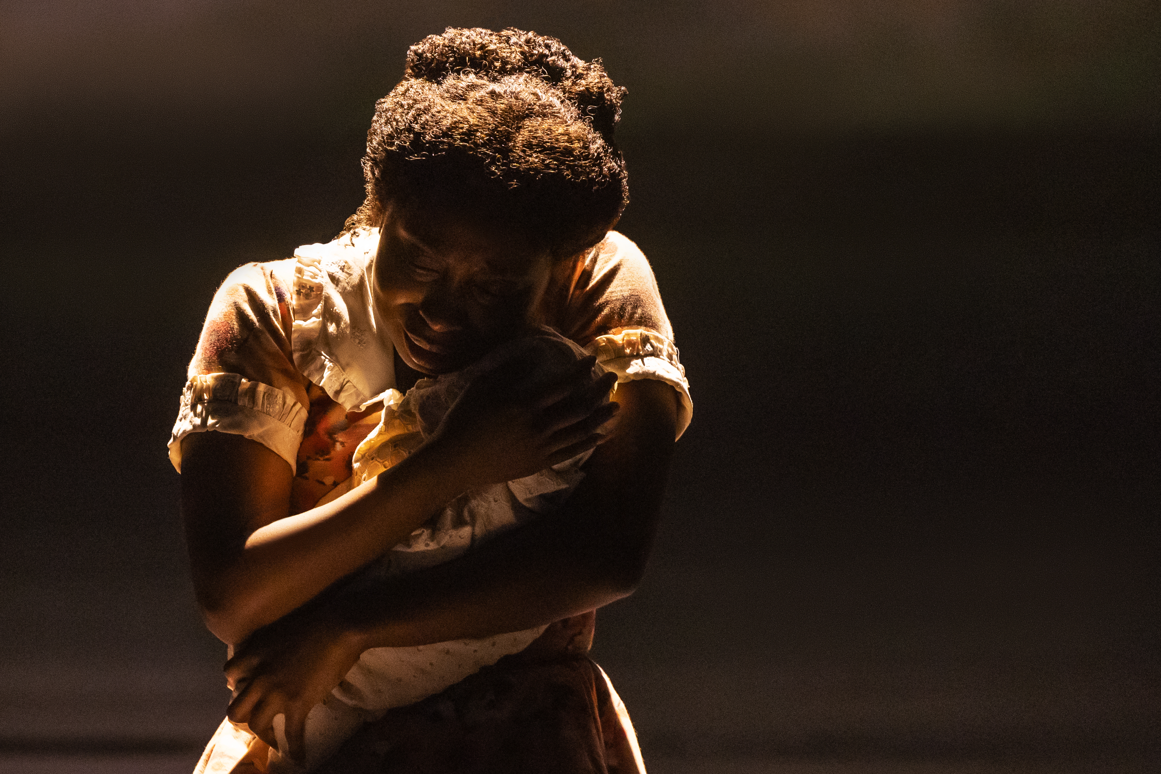 nichelle lewis holding a baby wrapped in a blanket on a dark stage in the broadway musical ragtime