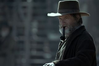 shea whigham as jim bridger smoking a pipe and wearing a cowboy hat in a still from american primeval