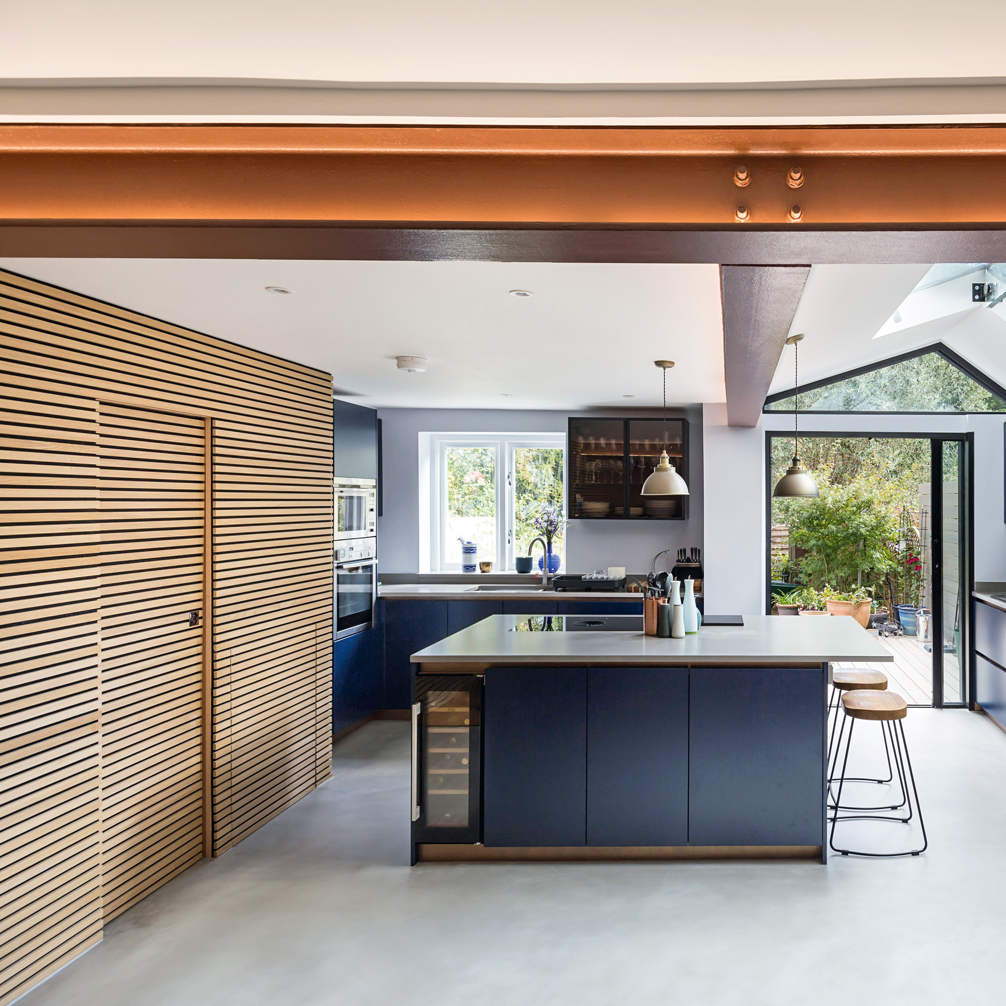 a kitchen with navy blue kitchen cabinetry. kitchen island and a copper coloured RSJ