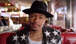Nick Cannon looking cool in a hat and jacket inside a diner.