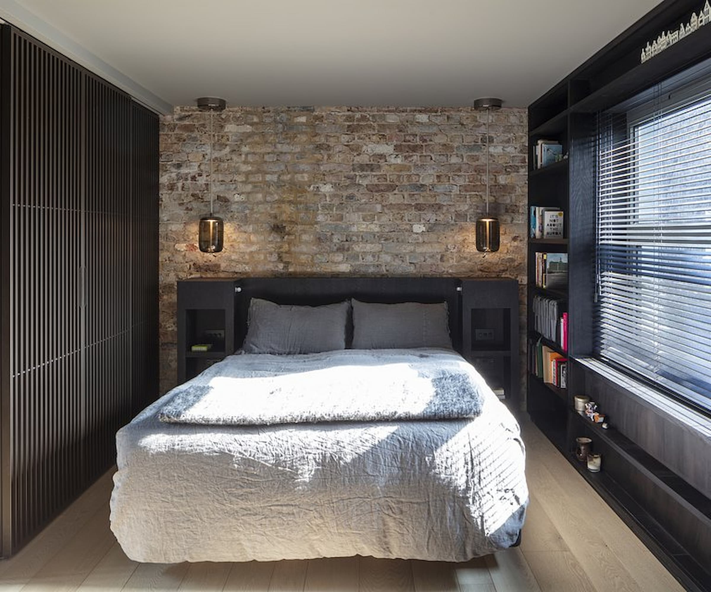 A bedroom with a brick back wall and black inbuilt wardrobe