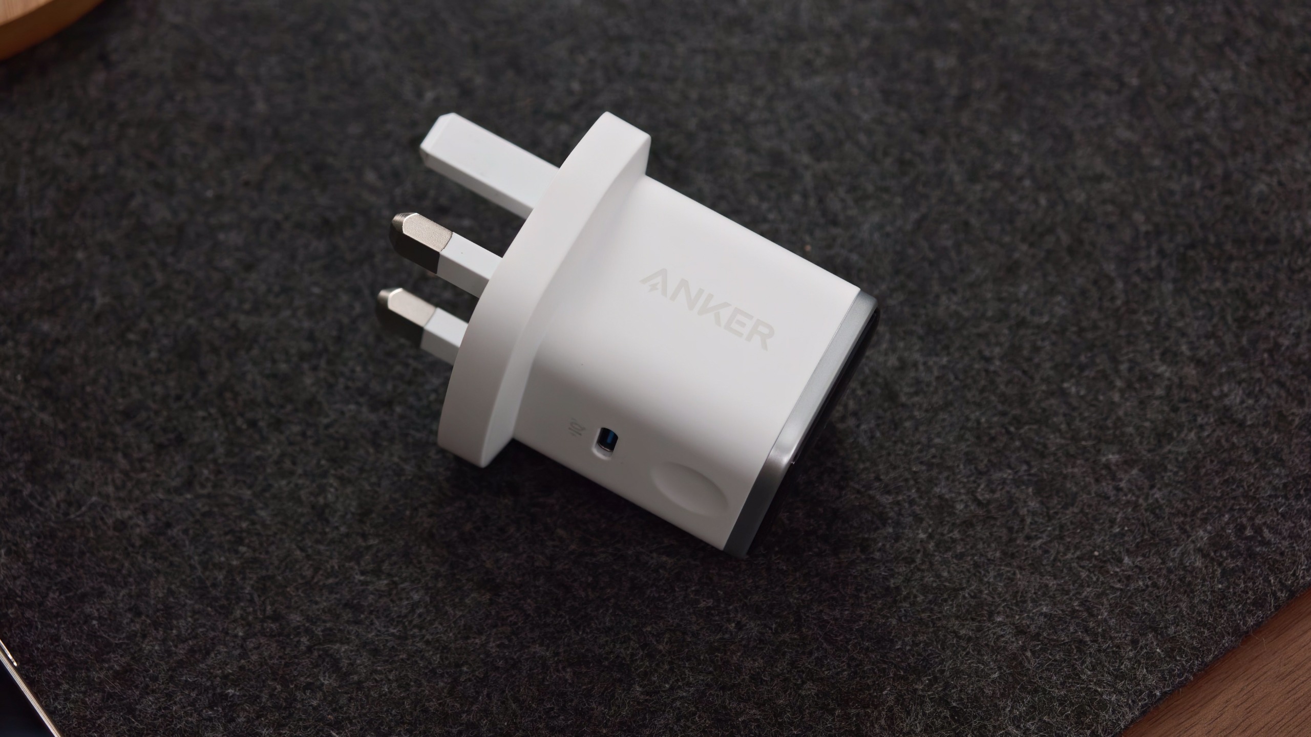 White Anker Nano Charger lying on a dark surface, showing the Anker logo, UK plug, and side button.