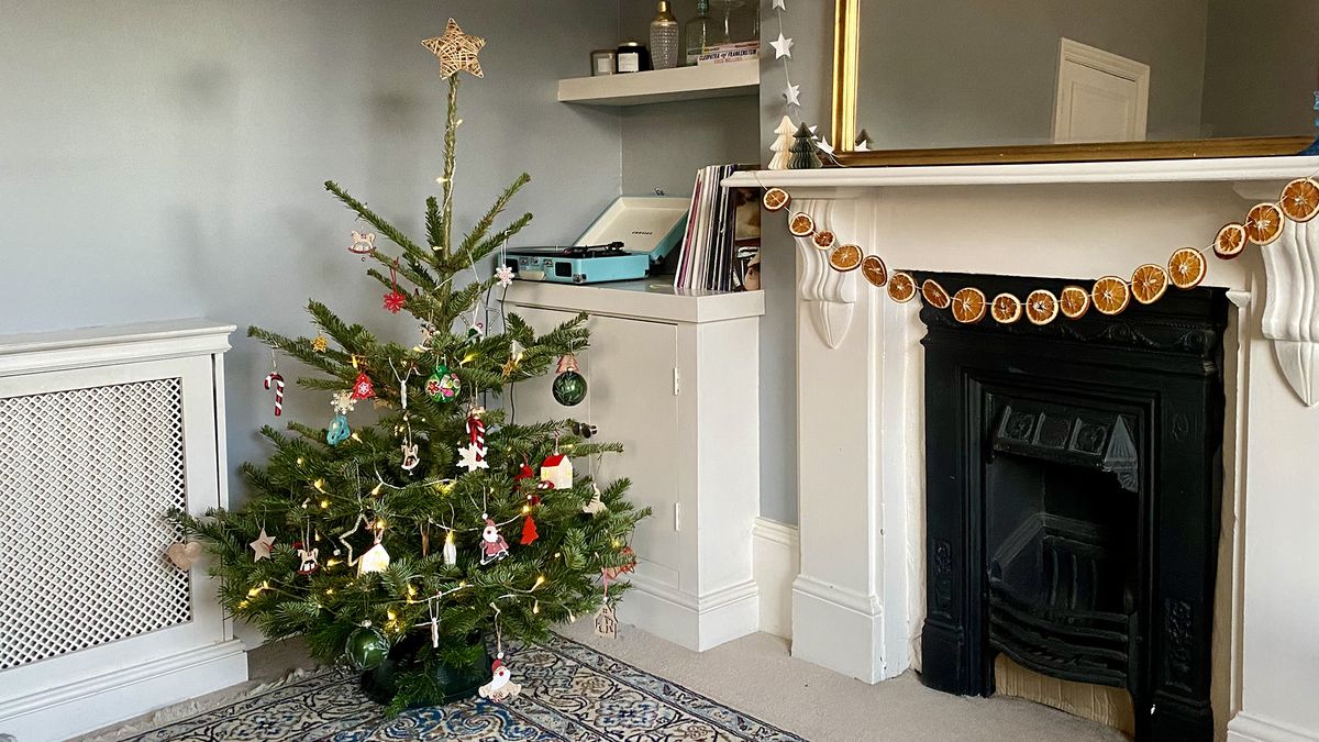 Christmas tree in a living room next to fireplace and orange garland.