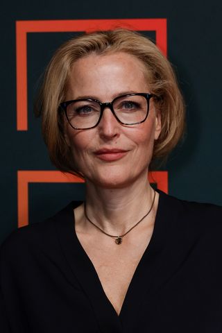 Image of Gillian Anderson wearing glasses and a black V-neck top with a faux blonde bob