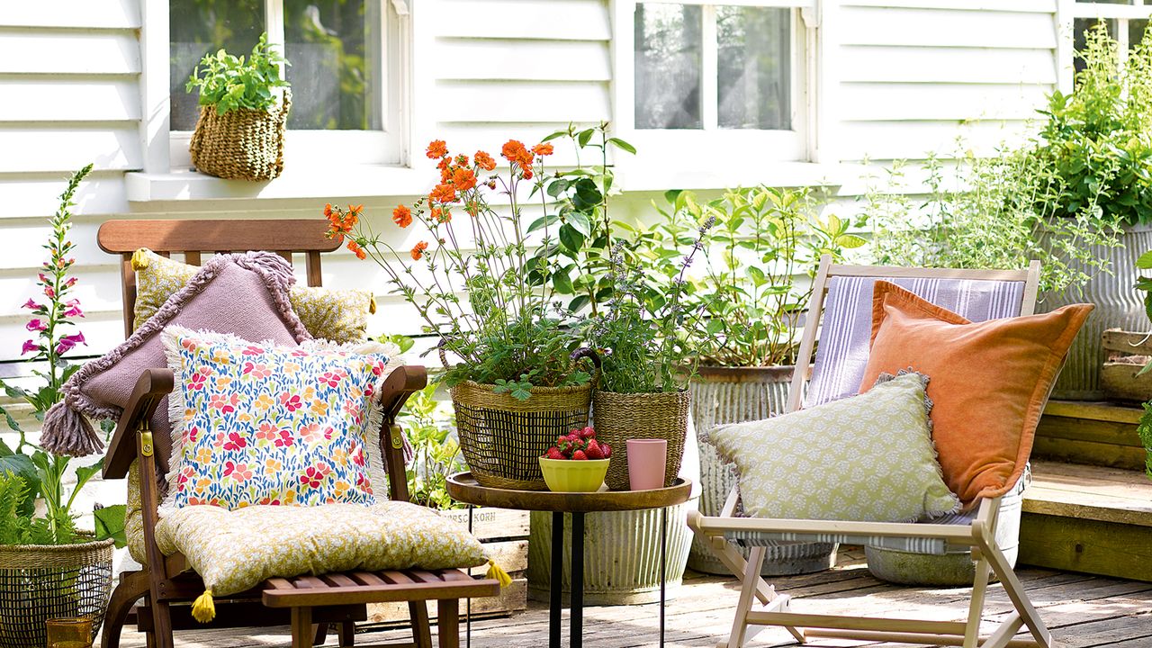 Two wooden deckchairs on decking surrounded by pots of flowering plants