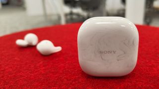 Sony LinkBuds Open earbuds charging case on red surface with earbuds in background