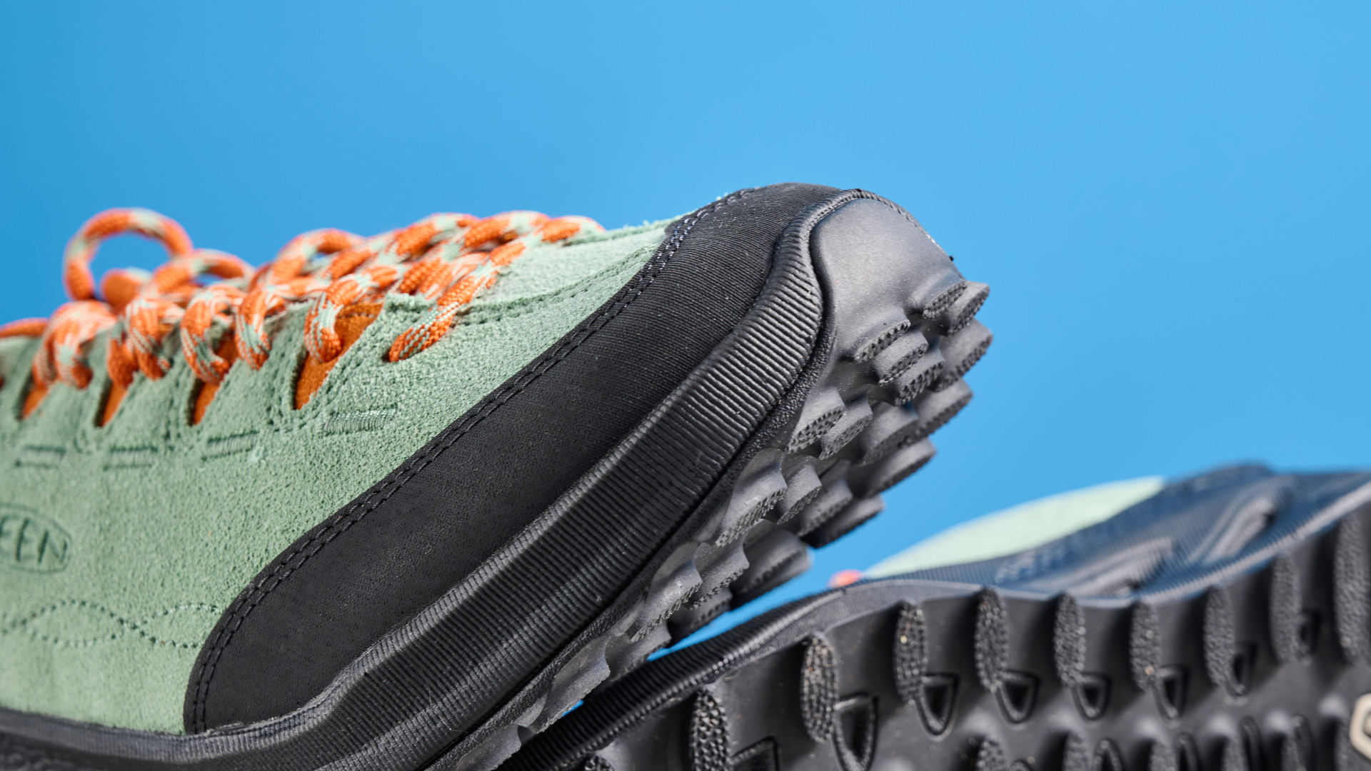 the keen jasper zionic hiking shoes in green/gold colorway photographed against a blue tom's guide background and a stone floor, showing the lug sole and the leather upper with orange laces