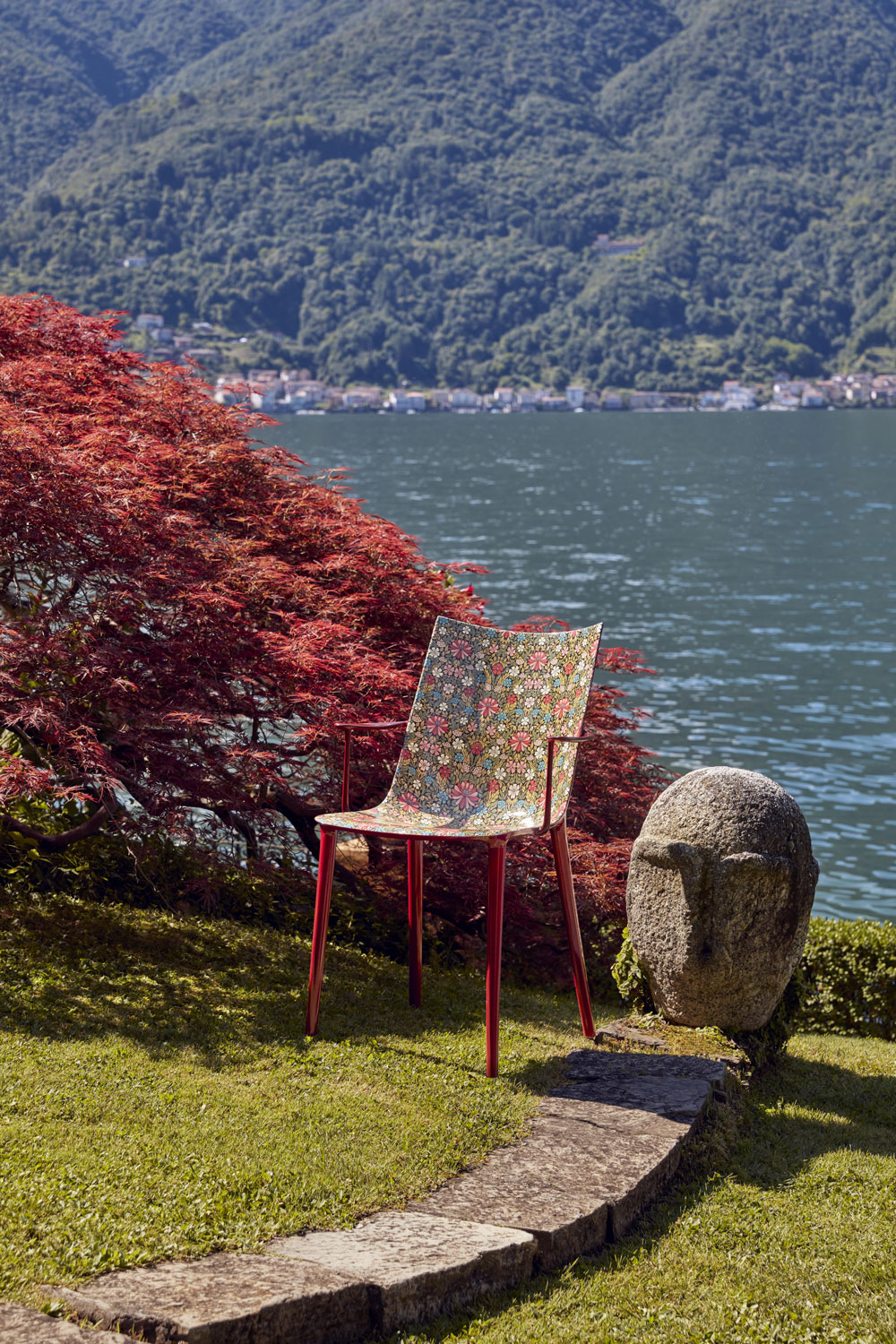 colourful patterned plastic chair on a lakeside lawn next to a maple tree