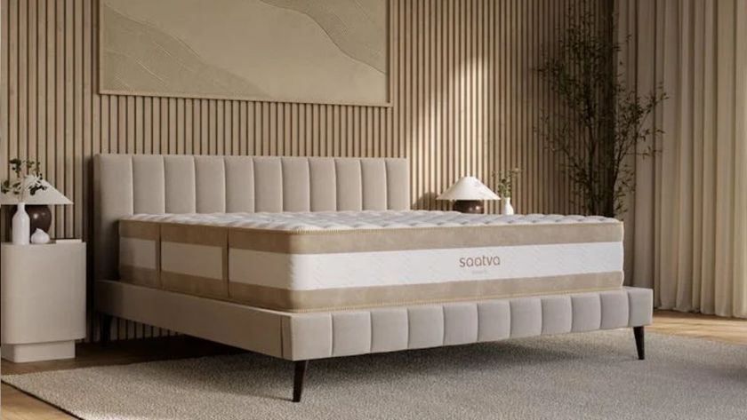 The image shows the cream and gold Saatva RX mattress on a beige bed frame in a neutrally decorated bedroom
