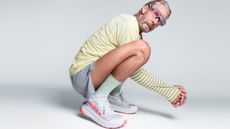 Altra athlete Peter Giles crouches down and looks at the camera, wearing Altra sneakers, shorts, a long-sleeved top and pink-tinged running sunglasses.