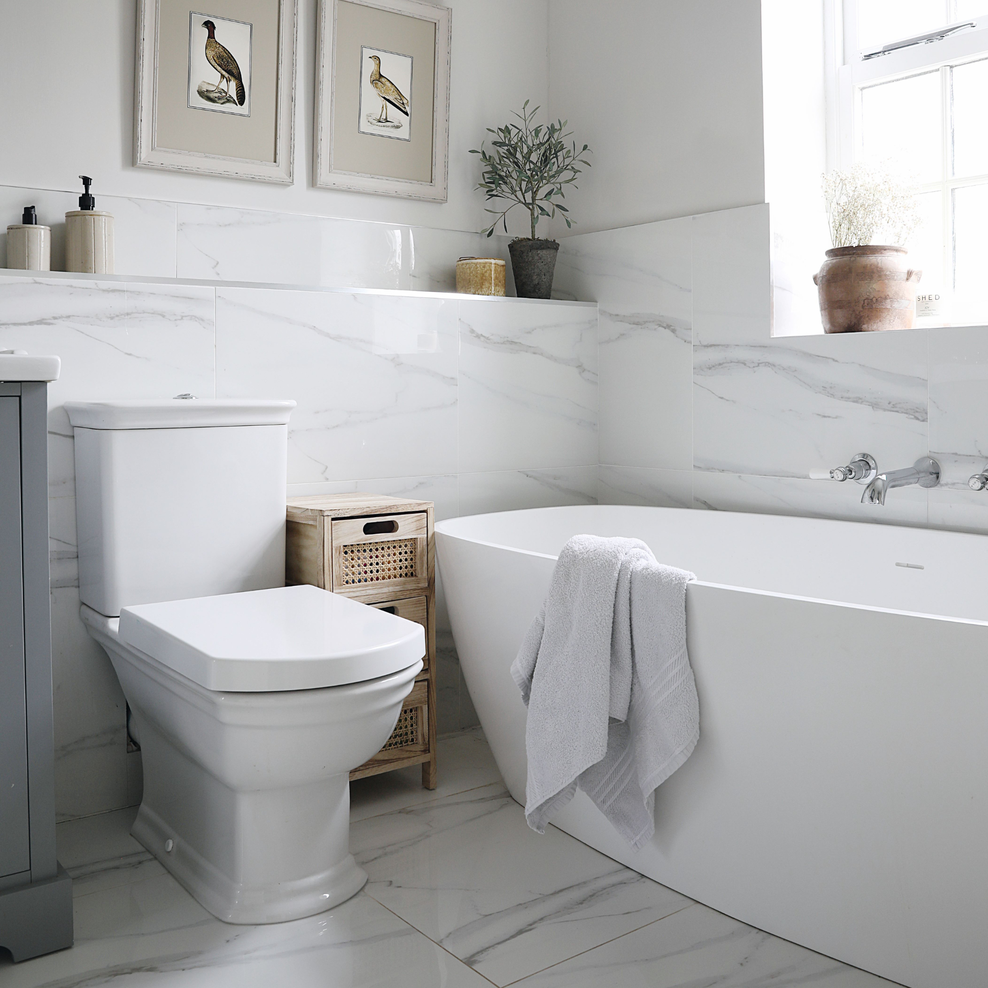White marble tiled bathroom with white bathtub and towel draping over
