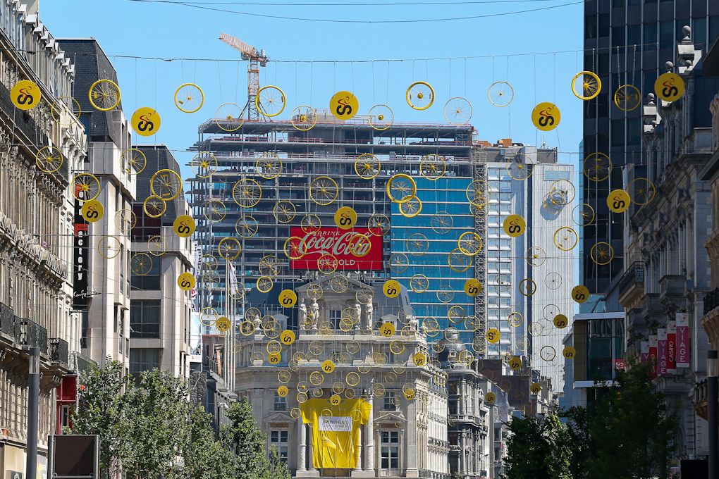 Tinsels with bicycle wheels hanging in a street with a giant Yellow Jersey hanging on a facade in Brussels centre