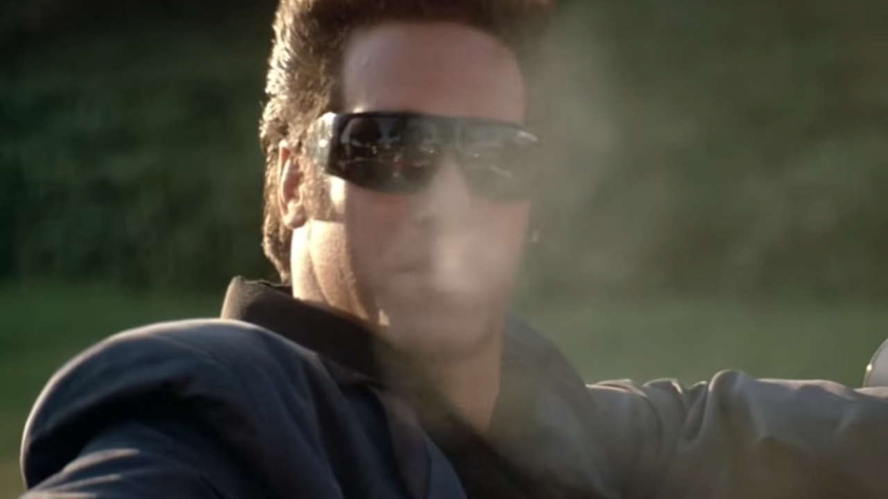 Andrew Dice Clay wearing sunglasses and blowing smoke into the camera.