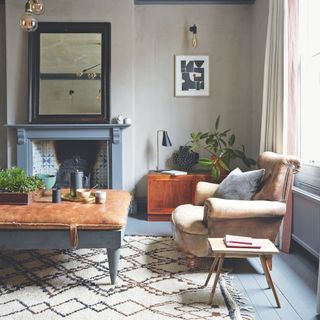 Grey living room with blue painted wooden floors, a leather armchair and a cream rug