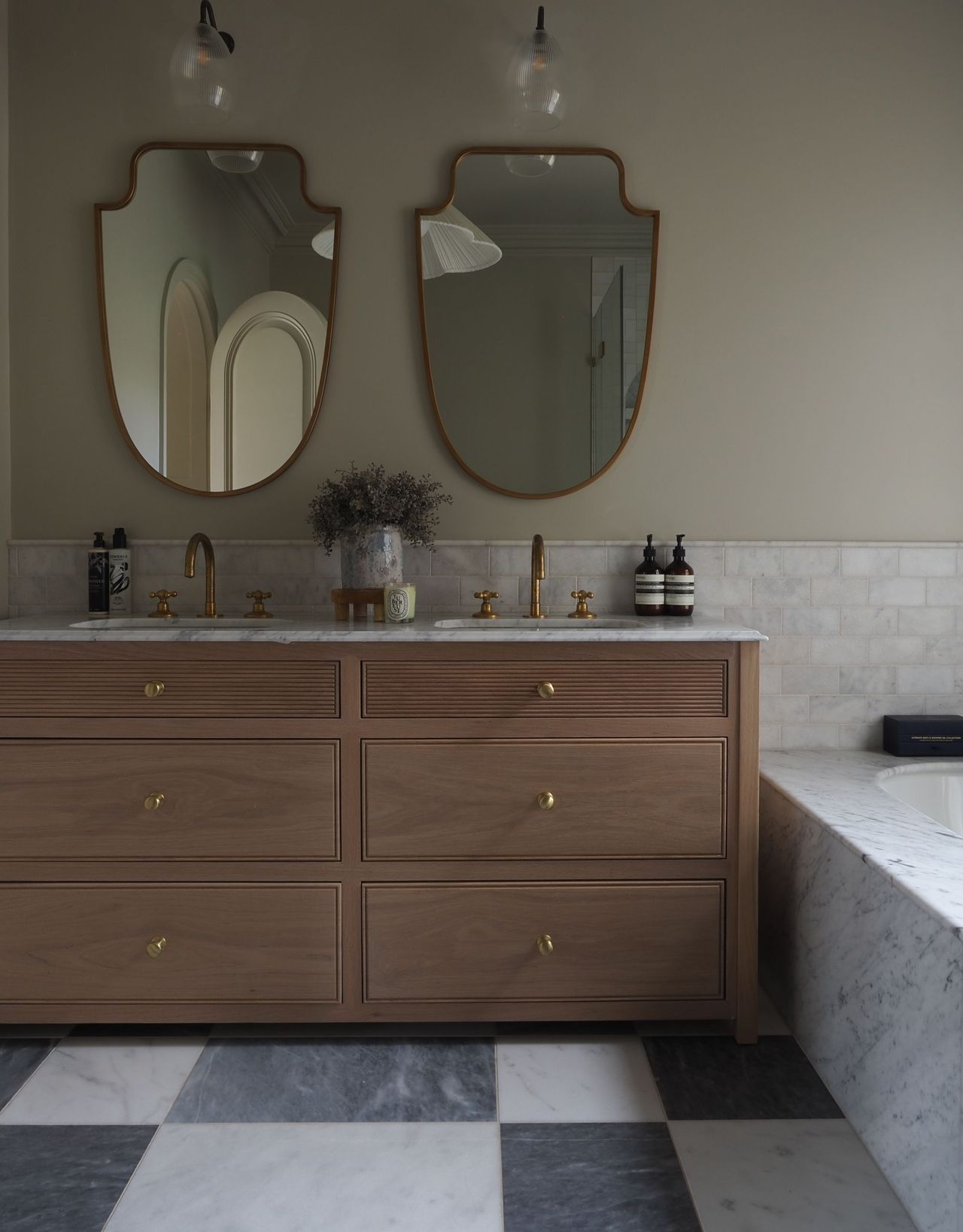A modern bathroom with a double vanity unit and double mirrors with wall lights above each of them, and brass taps and door knobs