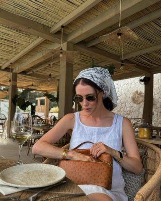 Woman wearing a white linen dress and a headscarf.