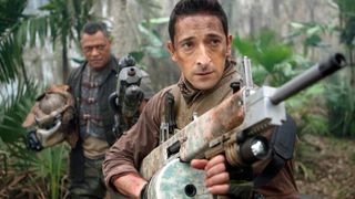 A still from the movie Predators in which Adrien Brody as Royce and Laurence Fishburne as Noland creep through the jungle with big guns.