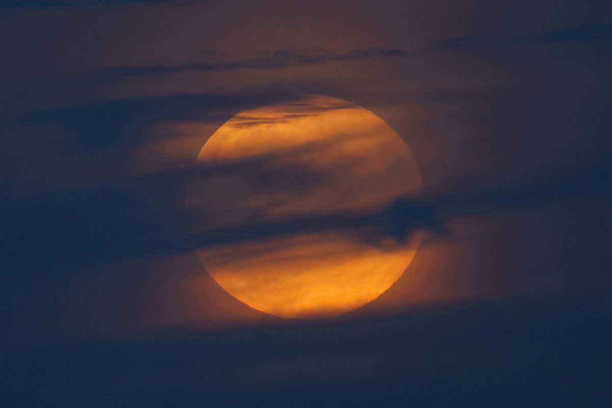 a fully, hazy moon hides behind wispy clouds