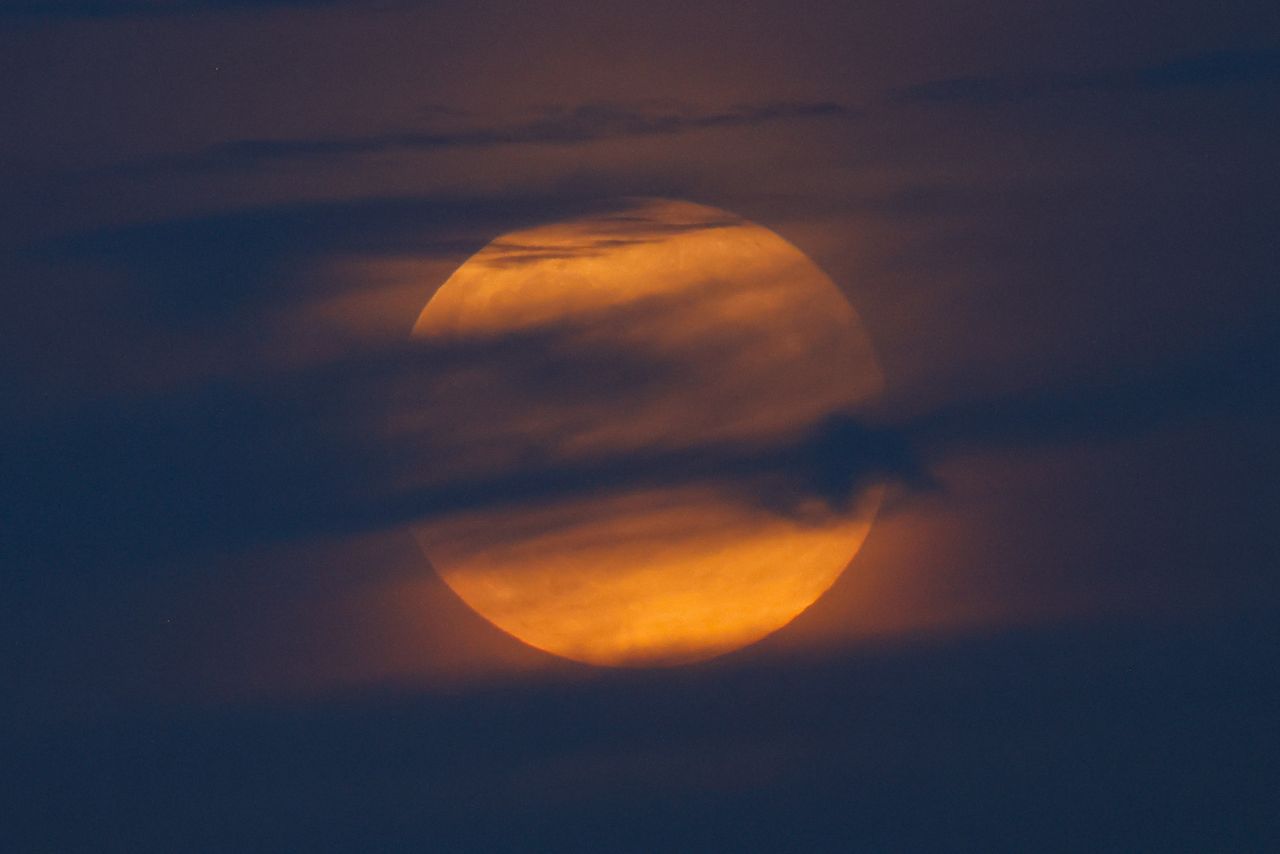 a fully, hazy moon hides behind wispy clouds