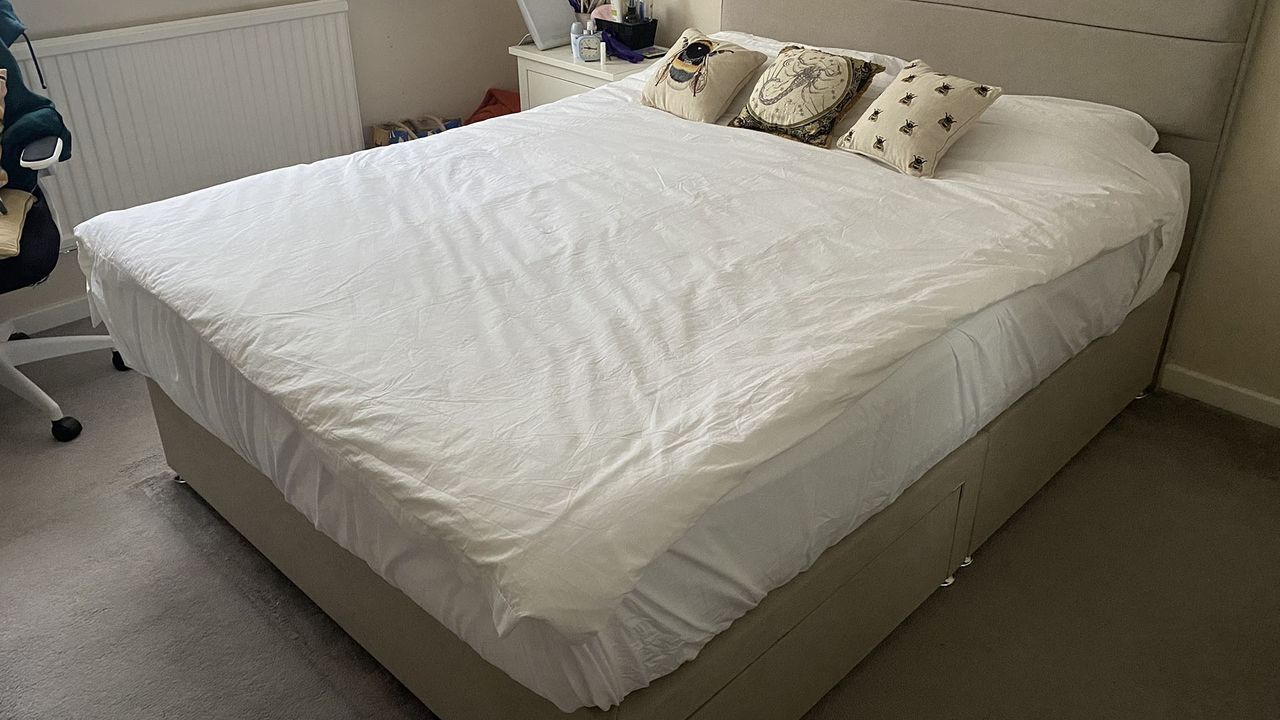 A queen size Siena Memory Foam Mattress on a divan bed frame in our reviewer's bedroom. The mattress is dressed in white bedding with a duvet and two pillow, plus three decorative cushions