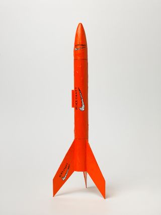 Model rocket, orange colour, black and white Nike crafty motifs on the nose body and tail, white background