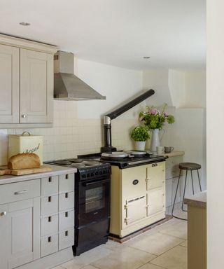 Beige kitchen with modern stove and oven next to old burning stove and oven with grey cupboards and drawers