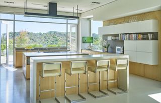 A kitchen with a white island and bar stools, white slab cabinetry, and a large floor to ceiling window with mountain views